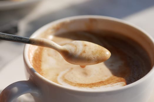 A stunningly beautifully swirled coffee presentation in a pristine white cup accompanied by a spoon