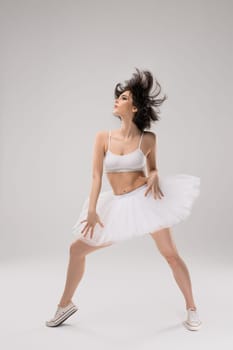 Beautiful charming ballerina in white suit posing on grey background
