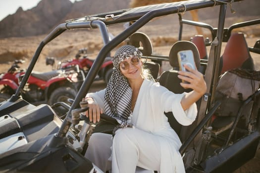 Woman tourist on ATV and ATV safari with desert background of Sharm el-Sheikh, Egypt taking selfie with background.