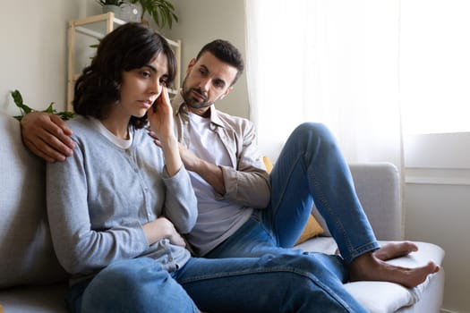 Man consoling sad wife sitting on the sofa at home living room. Copy space. Lifestyle concept.