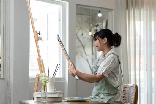 Young female artist works on abstract acrylic painting on canvas in art painting studio..