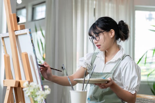 Young female artist works on abstract acrylic painting on canvas in art painting studio..