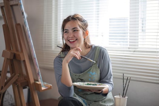 Portrait of a young female artist working on an abstract acrylic canvas painting in an art painting studio..