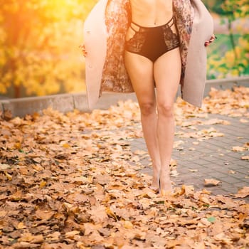 Young beautiful dark-haired woman with a slender figure posing in lingerie and a classic coat in an autumn park