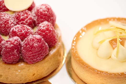 Close-up view of French desserts - a lemon and raspberry meringue cake and tartlet on a white plate. Still life. French traditional patisserie