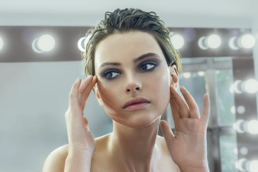 Young woman with makeup near illuminated mirror indoors.