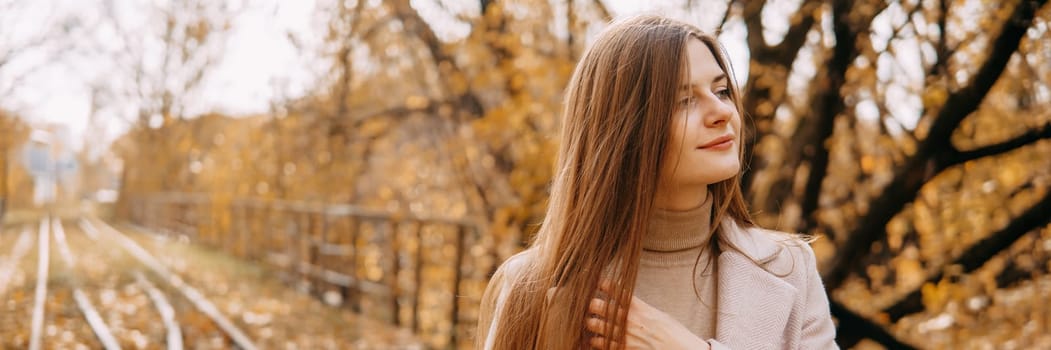 A beautiful long-haired woman walks through the autumn streets. Railway, autumn leaves, a woman in a light coat.