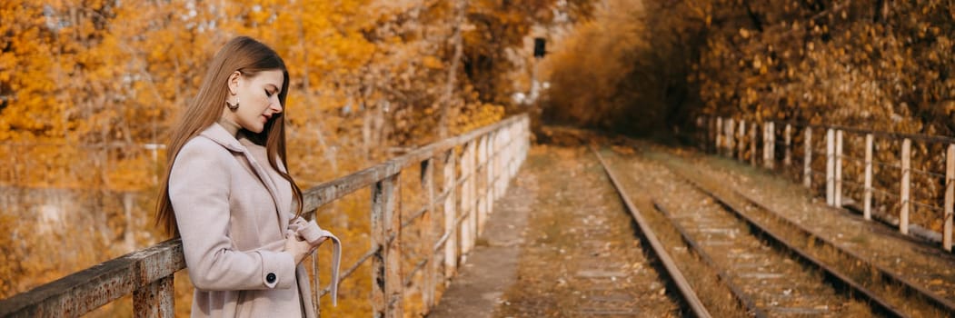 A beautiful long-haired woman walks through the autumn streets. Railway, autumn leaves, a woman in a light coat.