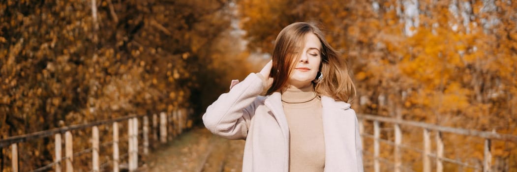 A beautiful long-haired woman walks through the autumn streets. Railway, autumn leaves, a woman in a light coat.