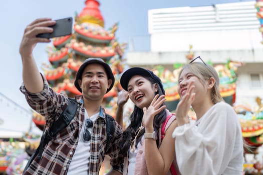 Three friends enjoy a lively festival capturing memories with smiles and selfies in a vibrant setting.