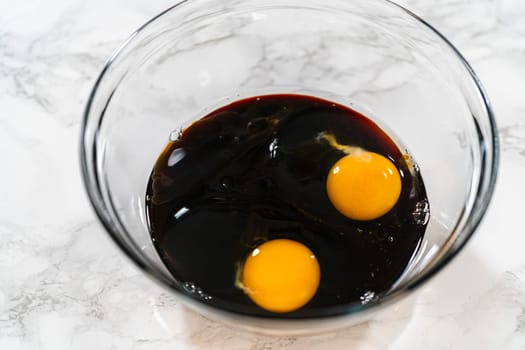 A top-down view of dark molasses and two eggs in a glass bowl, part of the wet ingredients for Zesty Orange Gingerbread Cookie Dough. The molasses adds depth and a rich color to the gingerbread.