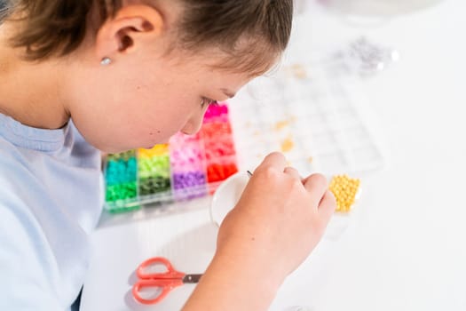 Little girl enjoys crafting colorful bracelets with vibrant clay beads set.