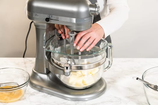 Front view of an electric stand mixer in use, blending ingredients for Classic Sugar Cookie Dough. The baker hands are steadying the bowl as the mixer combines butter, sugar, and other ingredients on a marble countertop