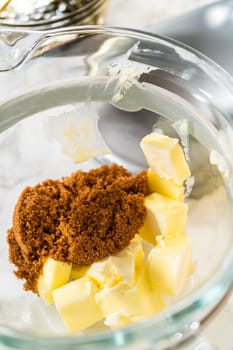 Butter and brown sugar are added to the mixing bowl, key ingredients for Chocolate Gingerbread Cookie Dough. These provide a creamy texture and deep sweetness, which complement the chocolate and spices.