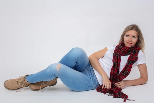 Adult beautiful slender woman in jeans and boots posing while lying in the studio.