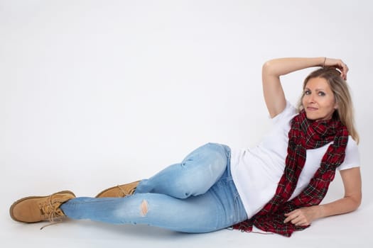 Adult beautiful slender woman in jeans and boots posing while lying in the studio.