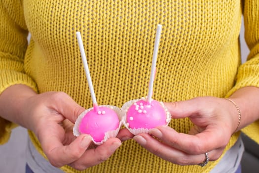 Hands hold two pink sweet candies on a stick.