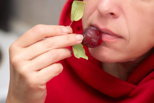 A woman, whose face is not visible, eats a small red wild apple.