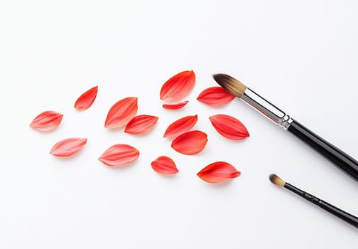 Delicate red petals scattered beside two paintbrushes on a clean white surface, showcasing a vibrant artistic display.