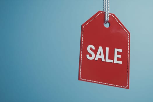 Red sale tag with white letters is suspended against a light blue background, emphasizing the discount opportunity for shoppers.