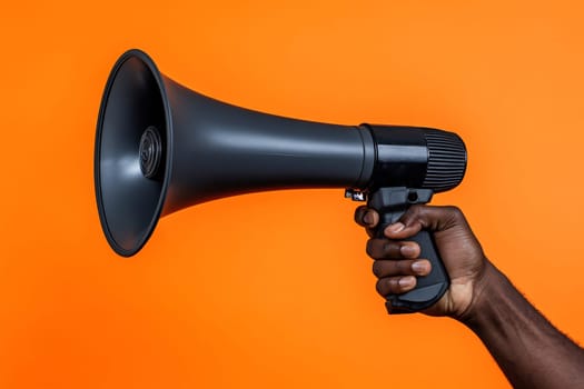 A person grips a black megaphone, ready to make an announcement, with a vivid orange backdrop enhancing the focus on the device.