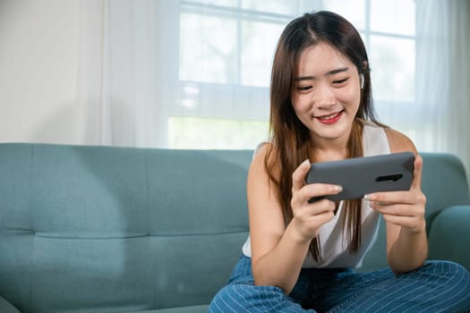 Social media networks. Asian young woman sitting on sofa using mobile smart phone at living room at home, happy beautiful female relax and shopping online with smartphone