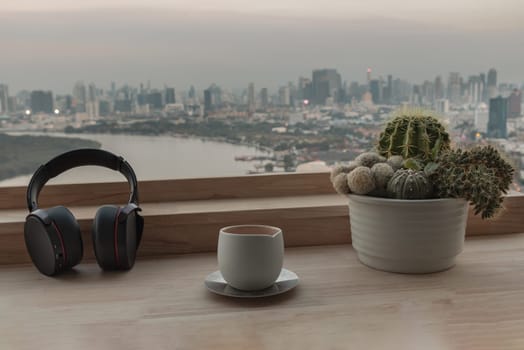 Bangkok, Thailand 02 Jan,2025 - Relaxation area or Working space in Condominium balcony overlooking river view. Ear headphones, Tea cup and Cactus pot on Wooden table, use it as your Wallpaper, Poster and Copy space, Selective focus.