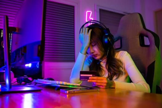 Young Asian woman gamer wearing headphones unset suffer of overspending money from card account after pay game online, problem using credit card, playing gaming with money