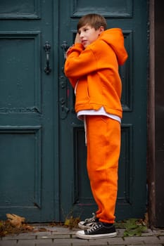 A teenage boy in an orange suit stands at the green door and eavesdrops.