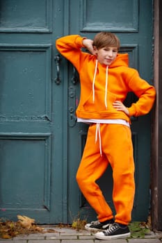 A teenage boy is standing in an orange suit near a green door.