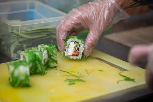 A gloved hand cuts sushi on a cutting board.