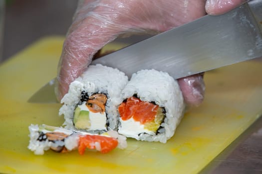 A gloved hand cuts sushi on a cutting board.