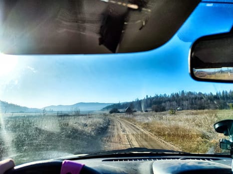 Car salon, windshield, steering wheel and landscape. View from seat of driver on nature with old road and village in the early morning with sun