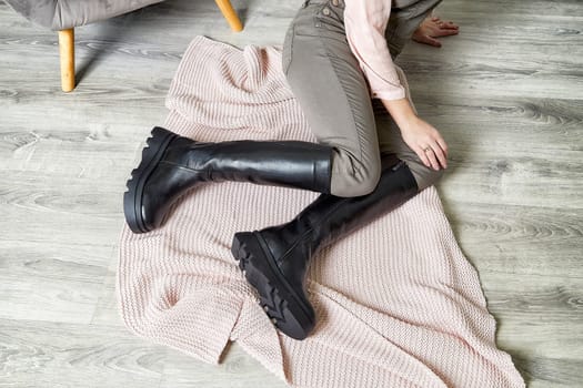 Fashionable model poses elegantly in a stylish outfit, highlighting trendy black knee-high boots and a soft blanket