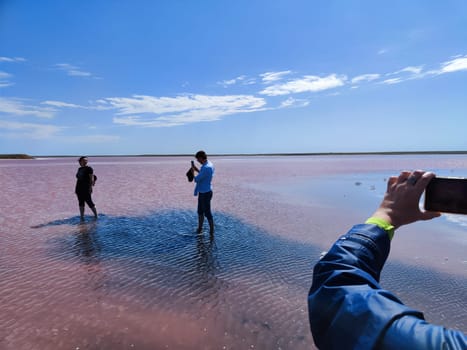 Elista, Russia - April 22, 2024: Visitors enjoy the stunning Pink Salt Lake in Kalmykia, Russia, capturing memories under clear blue skies with water reflecting the vibrant hues.