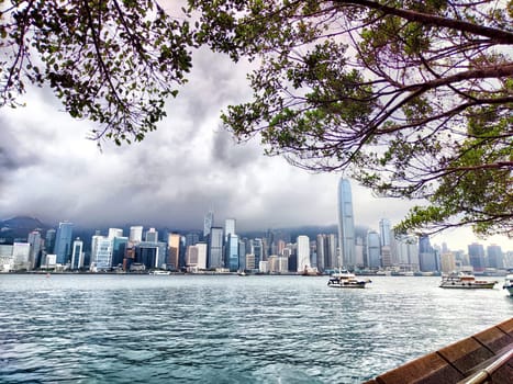 Hong Kong - April 06, 2024: Victoria Bay showcases a foggy skyline of Hong Kong with modern buildings partly obscured by clouds, creating a serene atmosphere on a quiet day. Boats float gently on the water.