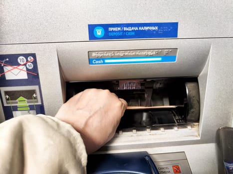Kirov, Russia - October 08, 2024: Hand reaching into an ATM slot to retrieve cash in a crowded setting, indicating a financial transaction.