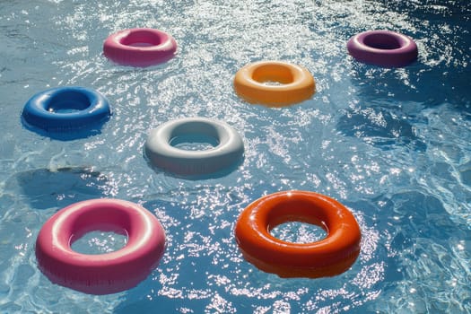 This vibrant image showcases colorful pool rings floating playfully on a tranquil blue water surface, reflecting sunlight beautifully. Perfect for summer themes!