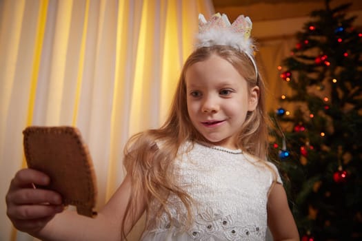 A young girl revels in the joy of the season, admiring a festive treat while surrounded by warm holiday decorations indoors.