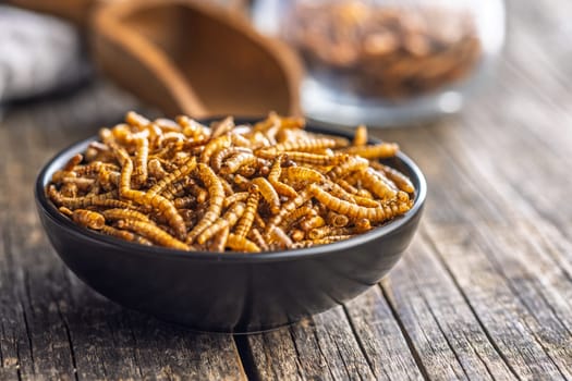 Dried salted worms. Roasted mealworms in bowl on a wooden table.