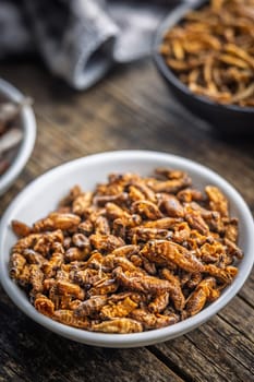 Dried salted insect. Roasted crickets in bowl on a wooden table.