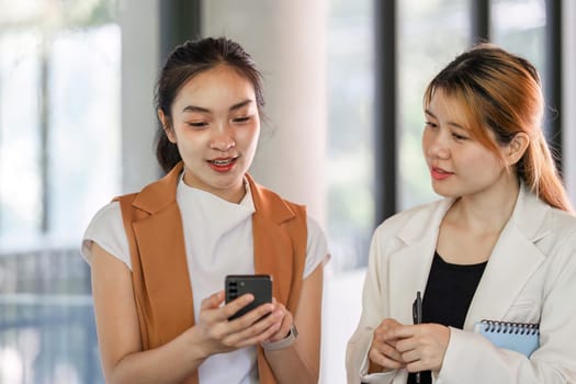 Two businesswomen collaborate and consult in a modern office setting, showcasing teamwork and professional interaction.
