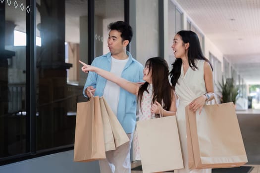 Smiling parents and their child enjoy a fun holiday shopping trip, carrying bags and exploring a modern mall.