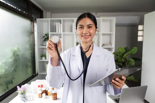 A confident female doctor in a white coat holds a stethoscope in a modern medical office, exuding professionalism and expertise.