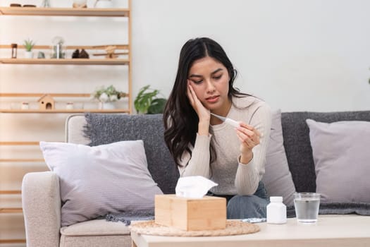A woman at home feels sick and unwell while checking her temperature reflecting the struggle of managing health.