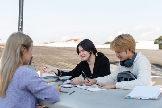 A group of students studying online together outside, using laptops and notebooks, fostering collaboration and learning in an outdoor setting.