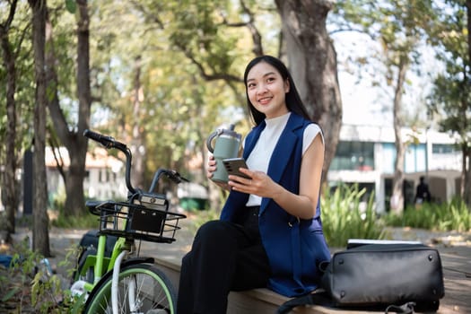 A young woman enjoys her bicycle ride sipping tea promoting clean energy and reducing pollution in a vibrant urban park.