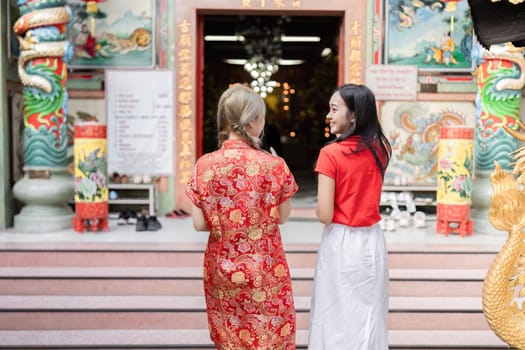 Two friends embrace the festive spirit of Chinese New Year at a lively temple dressed in traditional attire celebrating together.