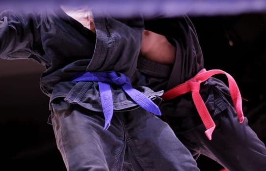 Man in dark kimono and blue belt training karate over dark background. 2 belts red and blue. Kimono for martial arts, sportswear, martial arts apparel