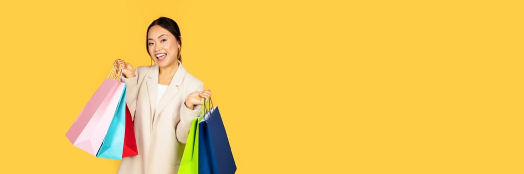 Joyful Asian millennial woman on shopping spree, her arms brimming with colorful bags, reflecting both delight of purchases and contemporary, consumer-oriented lifestyle of young adults today